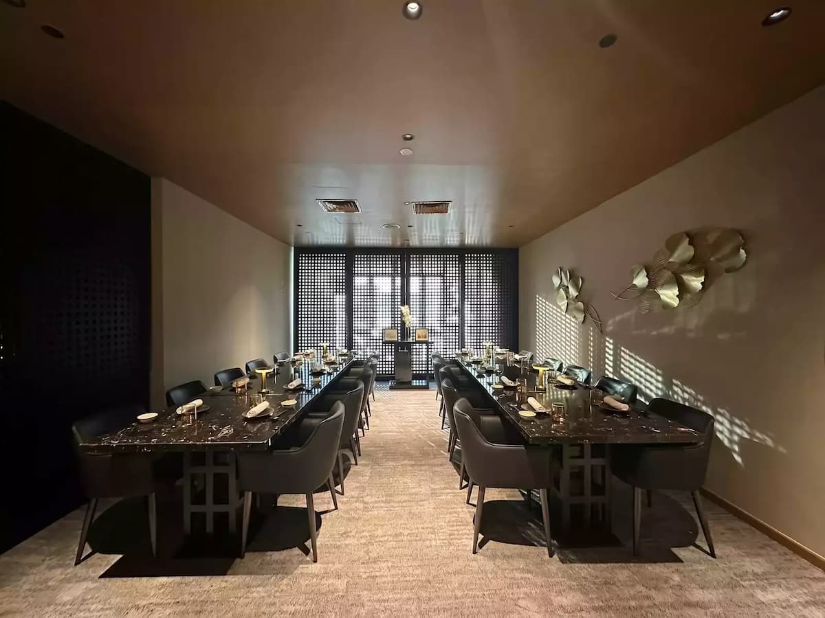 A wide-angle view of a sophisticated, narrow dining room featuring two long, parallel black marble tables.