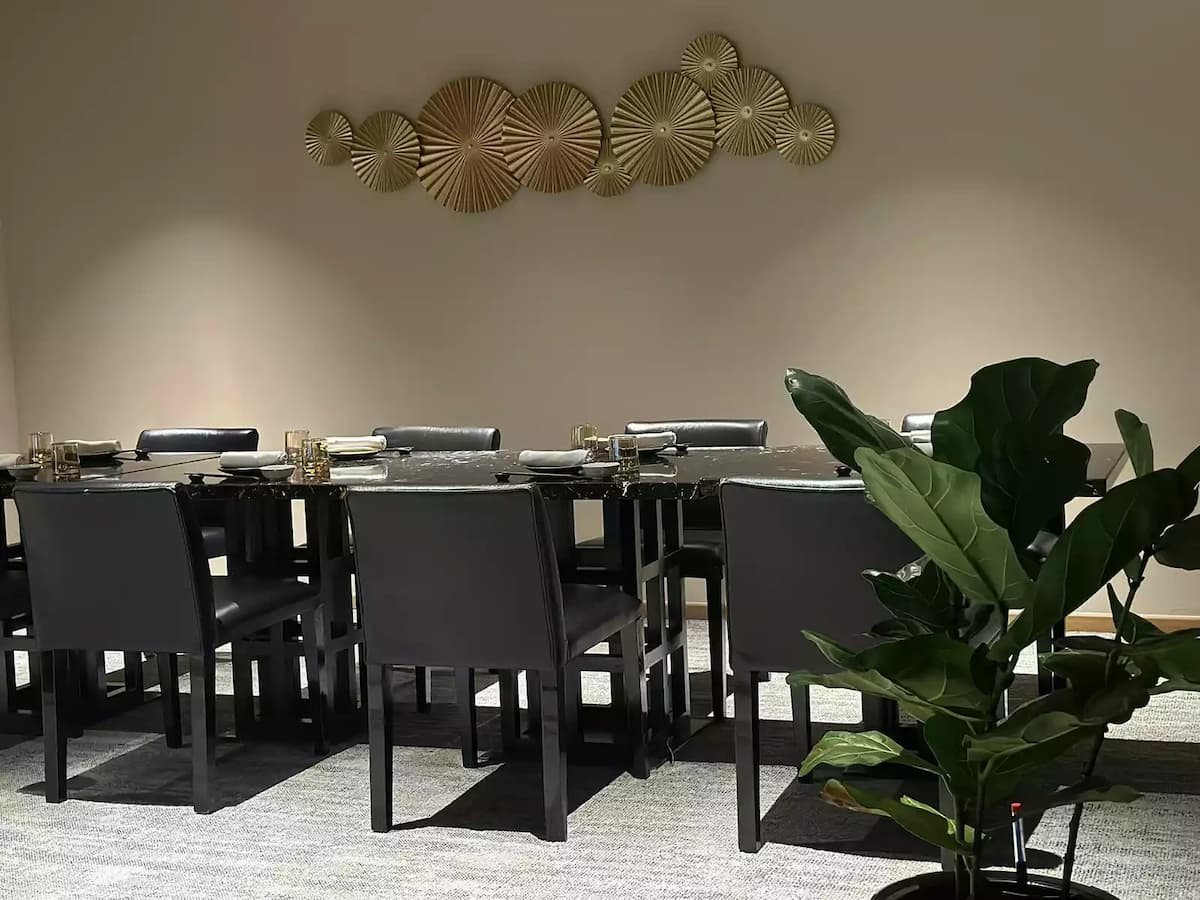 a modern dining room, a long, black marble table is surrounded by sleek black chairs and set with elegant glassware and linens.