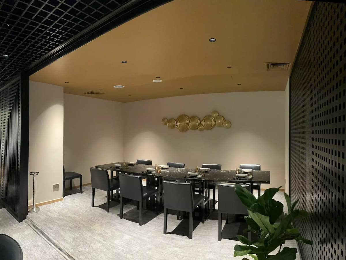 modern private dining room, a long, black marble table is set with sleek black chairs under warm, recessed ceiling lights.