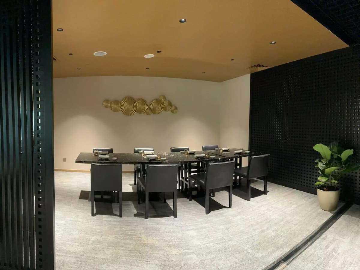 a modern private dining room, a long black marble table set with grey upholstered chairs is centered under warm ceiling lights.