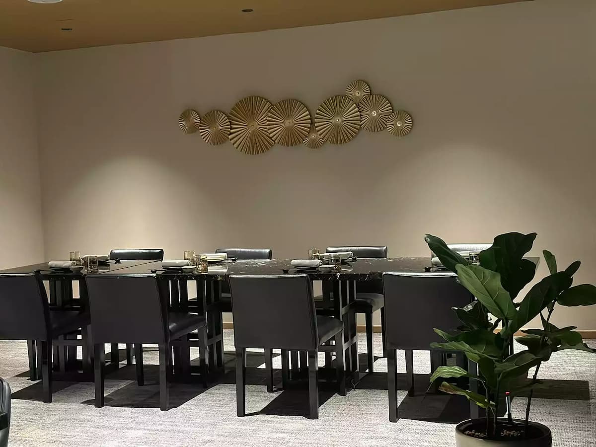 An elegant restaurant dining room featuring two long, parallel black marble tables set with modern tableware and glowing orb-like lamps.