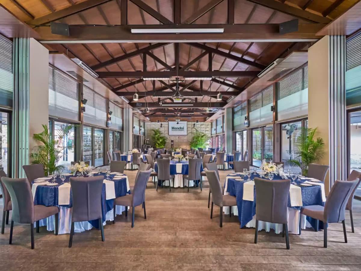 Rustic indoor venue with timber beams, round dining tables, and garden views.