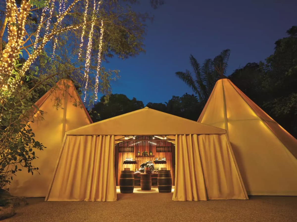 Teepee-style outdoor event tent with warm lighting and bar setup at night.