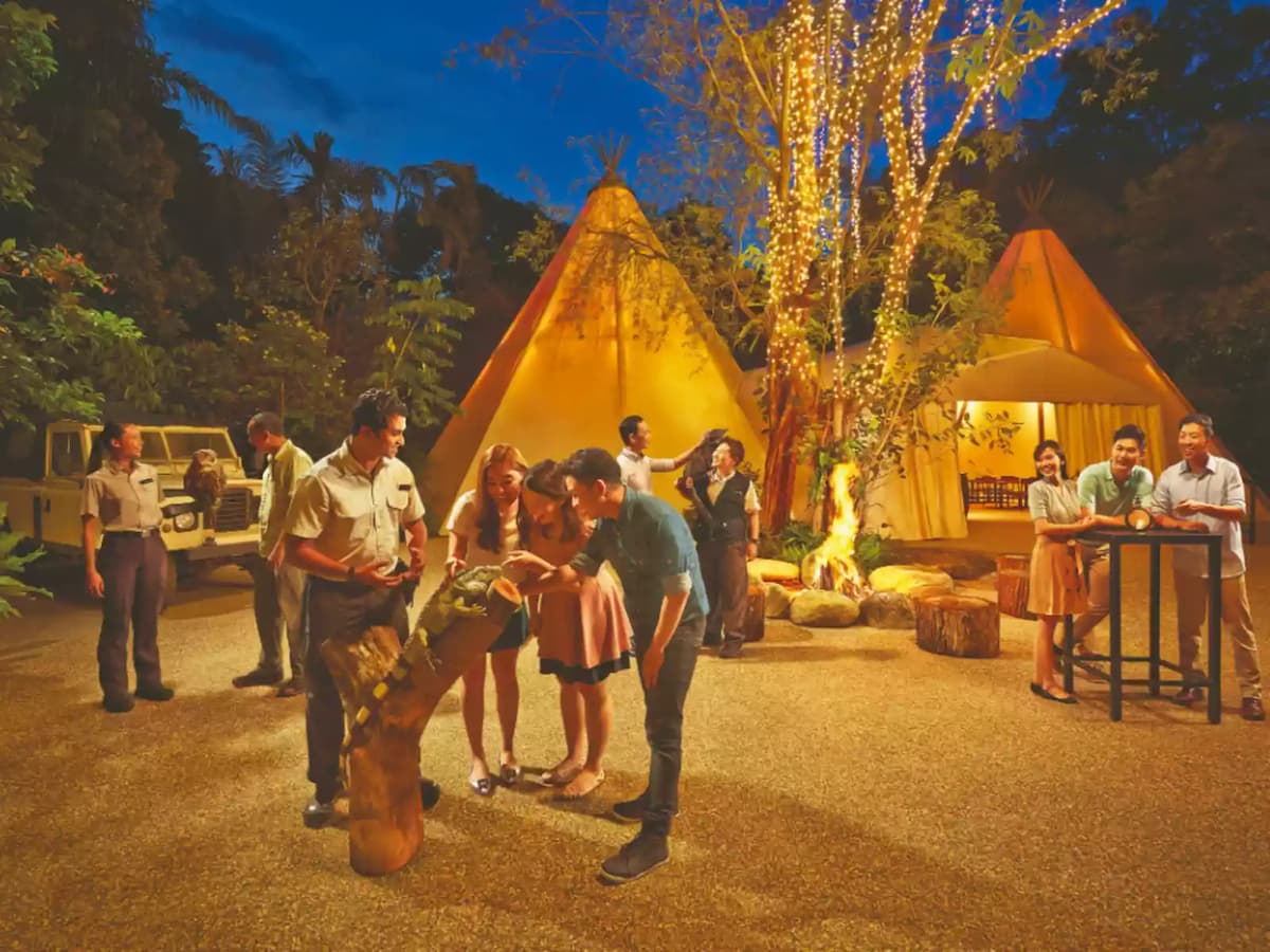 Outdoor evening event with teepee tents, fairy lights, and guests around a campfire.
