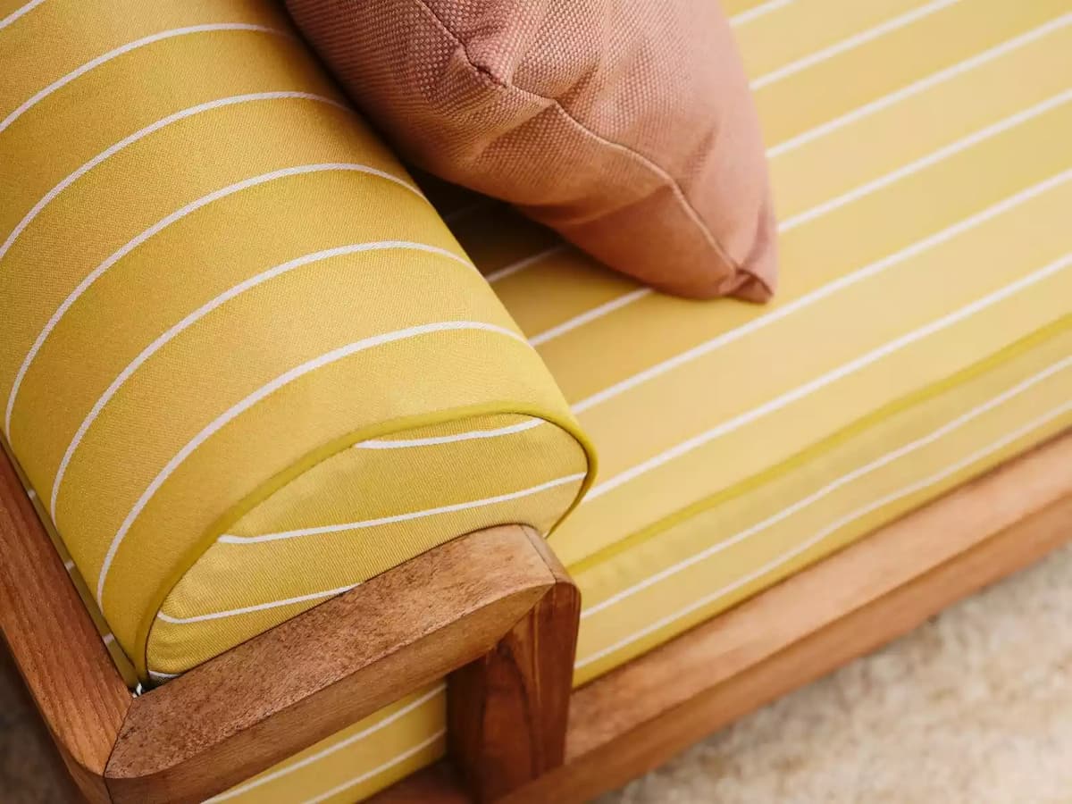 Close-up of yellow striped cushion on a wooden lounge chair with a peach accent pillow.