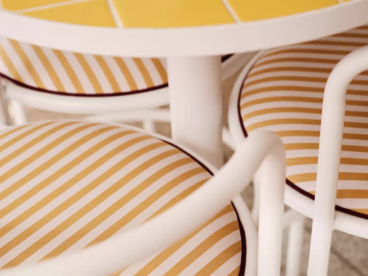 Close-up of white chairs with yellow-and-white striped cushions around a round table.