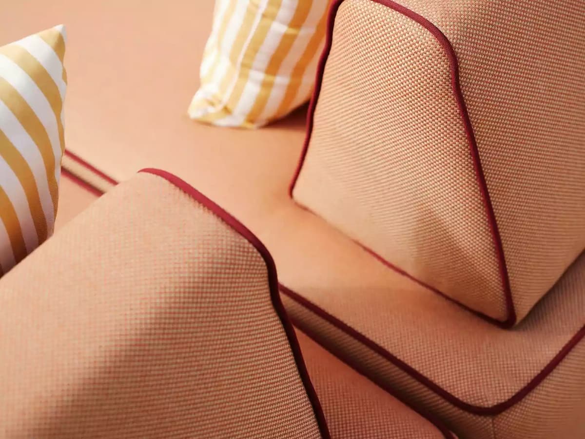 Close-up of peach-colored sofa cushions with red piping and striped accent pillows.