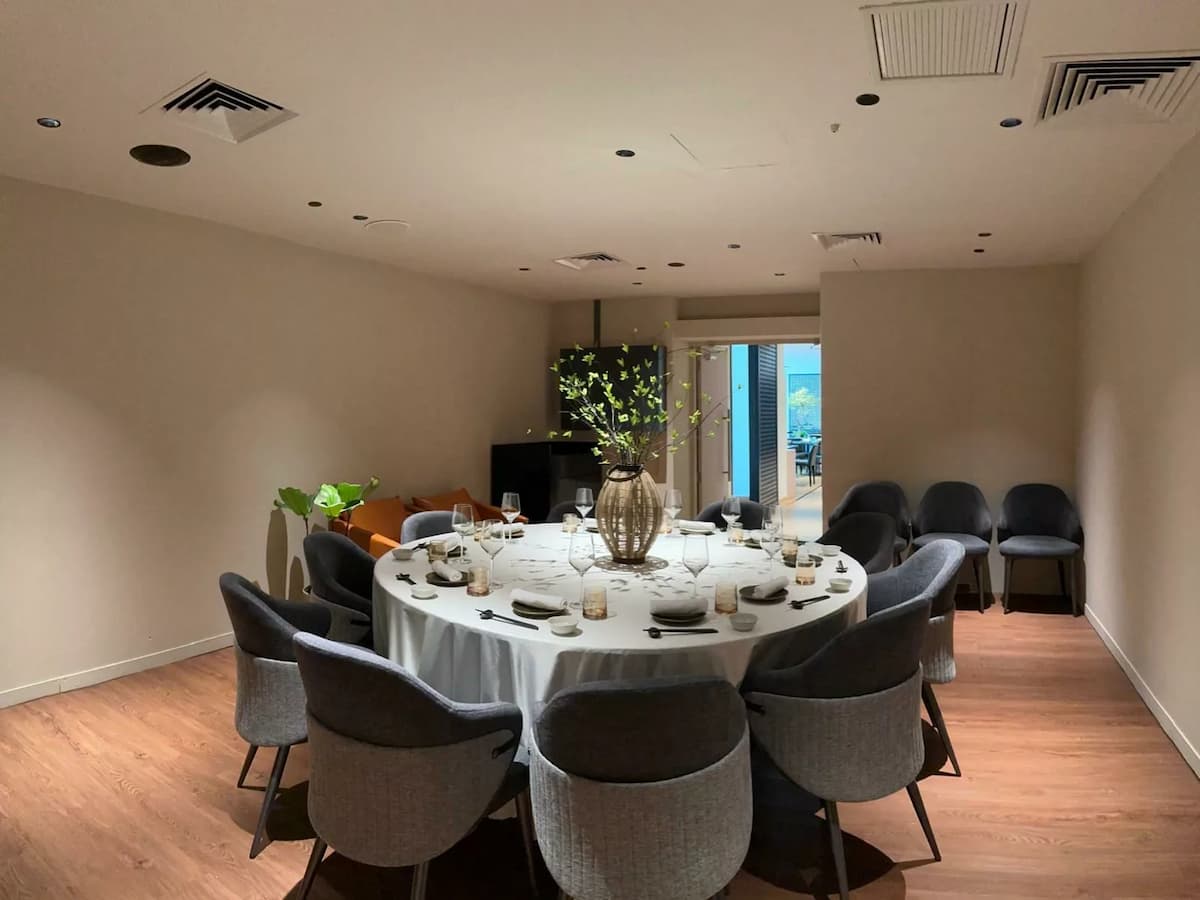 An elegant restaurant table setting features crystal wine glasses, rolled white linens, and dark ceramic plates on a polished black surface.