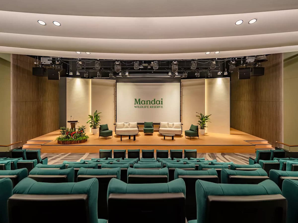 Auditorium with stage lounge seating, presentation screen, and tiered chairs.