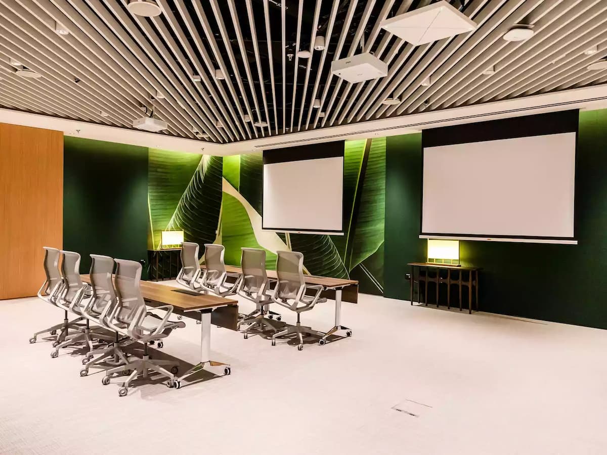 Modern meeting room with dual screens, movable tables, and ergonomic chairs.