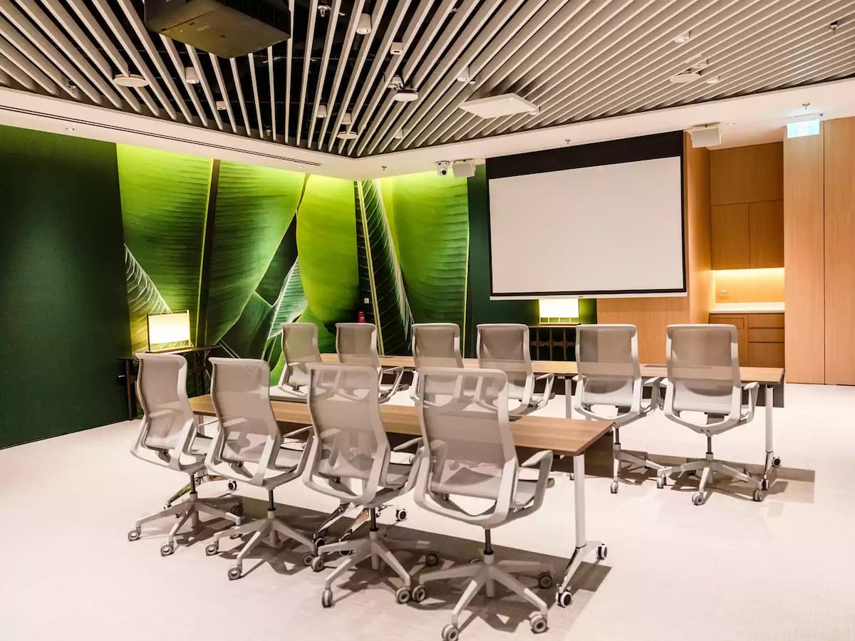 Contemporary boardroom with conference table, ergonomic chairs, and presentation screen.