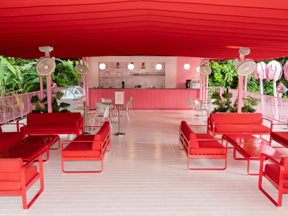 Open-air pink café space with red lounge seating, bar counter, and greenery surrounding the terrace.