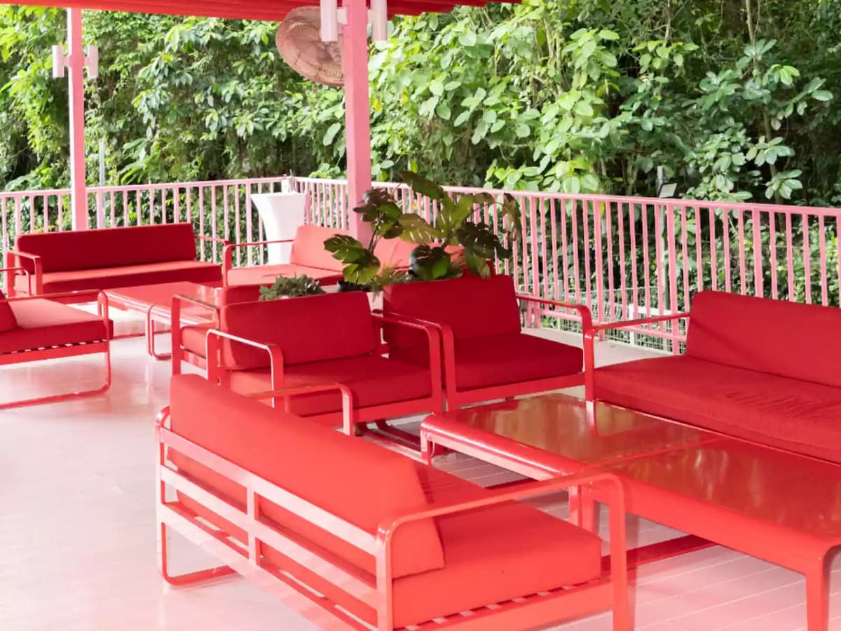 Covered outdoor terrace with bright red lounge seating and greenery in the background.