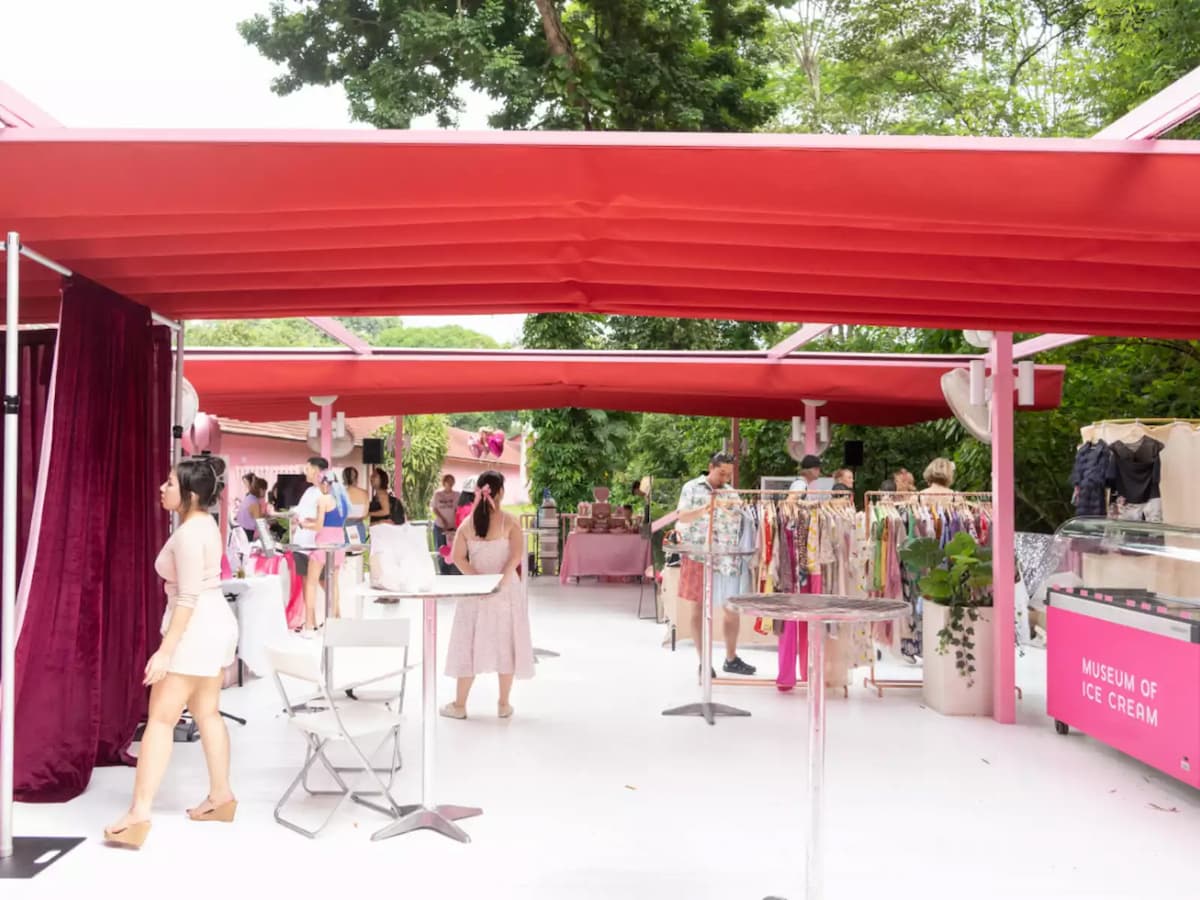 Outdoor pop-up market under red canopies with clothing racks, display tables, and visitors browsing.