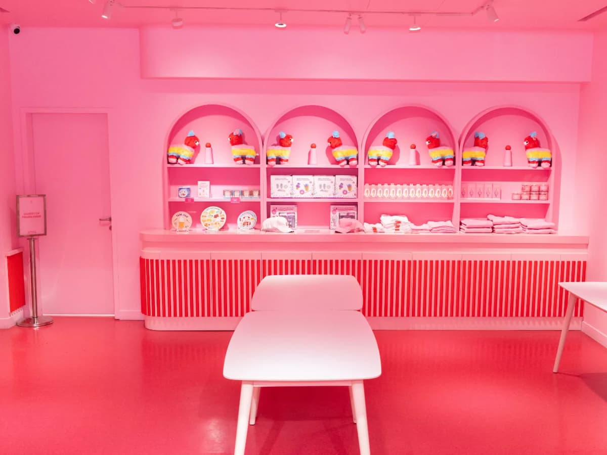 Bright pink retail space with arched shelves of colorful merchandise and a white bench centered in front.