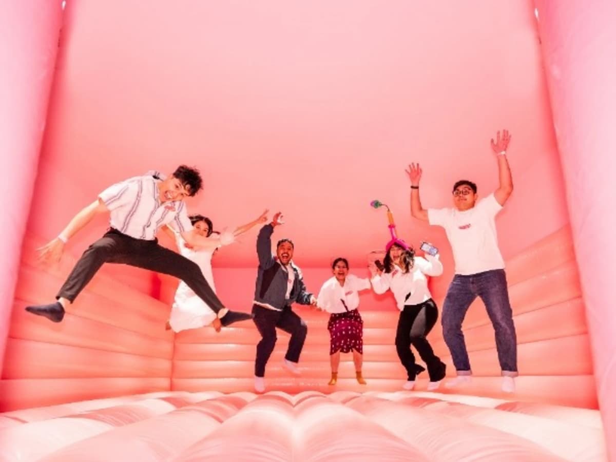 Group of people jumping inside a bright pink inflatable room, laughing and posing playfully.