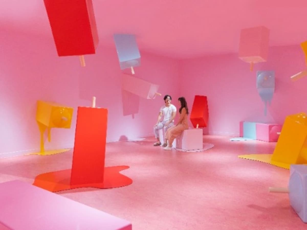 Pink immersive room with oversized melting popsicle sculptures and two people seated on a bench.