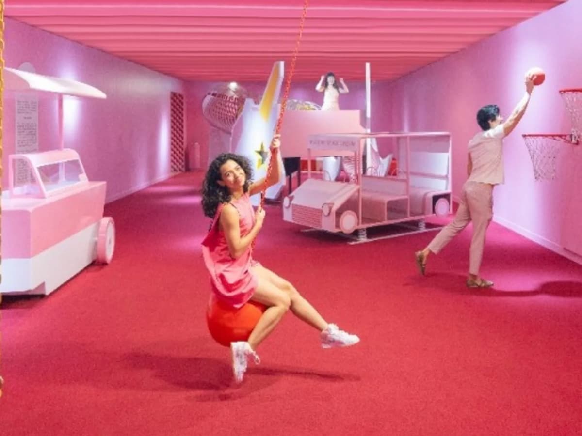 Playful pink indoor space with people posing on swings and near basketball hoops, surrounded by themed props.