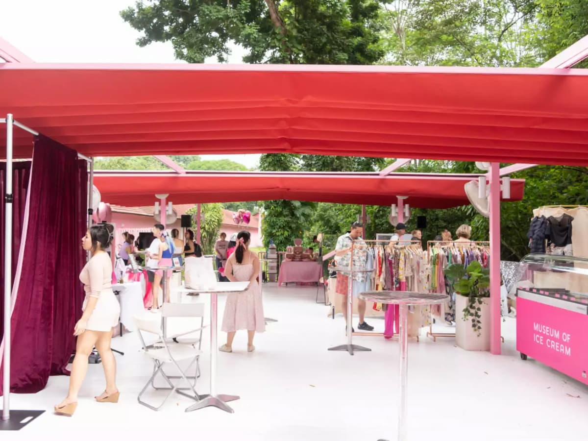 Outdoor pop-up market under red canopies with clothing racks, tables, and visitors browsing.