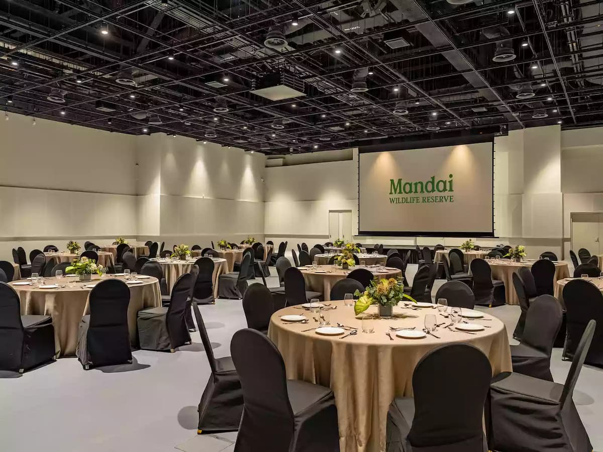 Banquet-style event hall with round dining tables and large presentation screen.