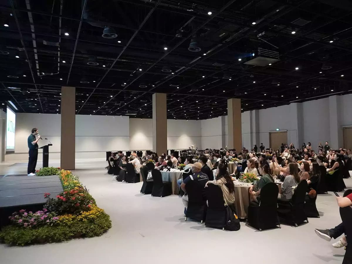 Large event hall with seated audience, round tables, and stage presentation.