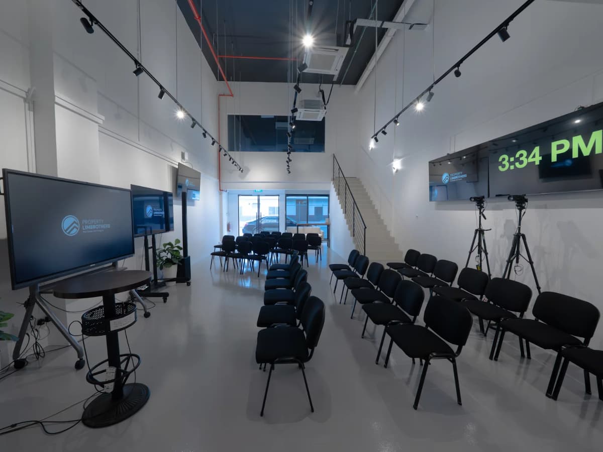Modern event space with rows of black chairs, large display screens, and a staircase leading to a mezzanine.