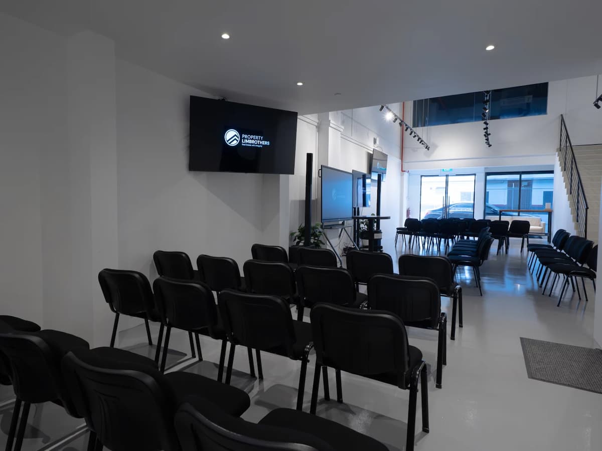 Modern event venue with rows of black chairs facing large display screens and natural light from the entrance.