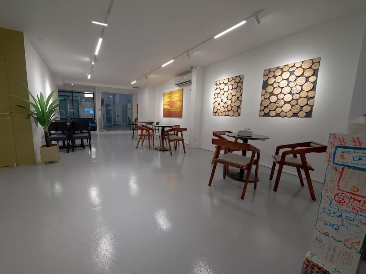Modern café interior with wooden chairs, small tables, artwork on white walls, and a mustard accent wall.