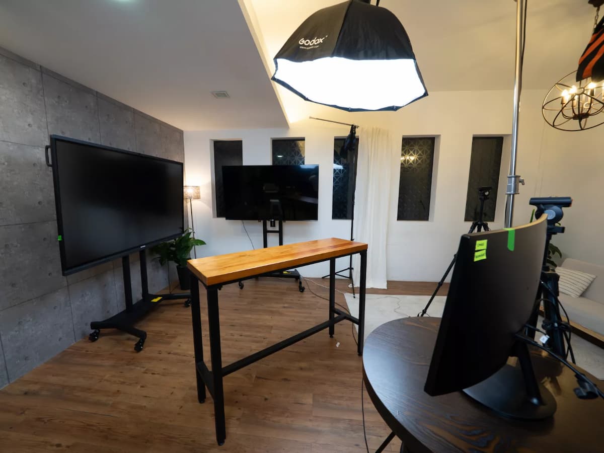 Compact studio setup with lighting equipment, large screens, cameras, and a wooden table on a wood floor.