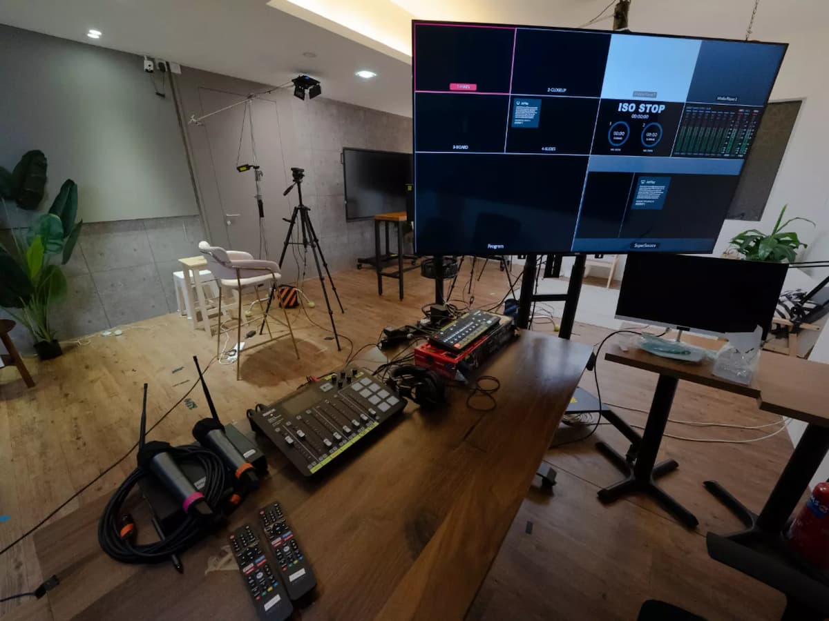 Behind-the-scenes production setup with video switcher, monitor display, cameras, and studio seating area.