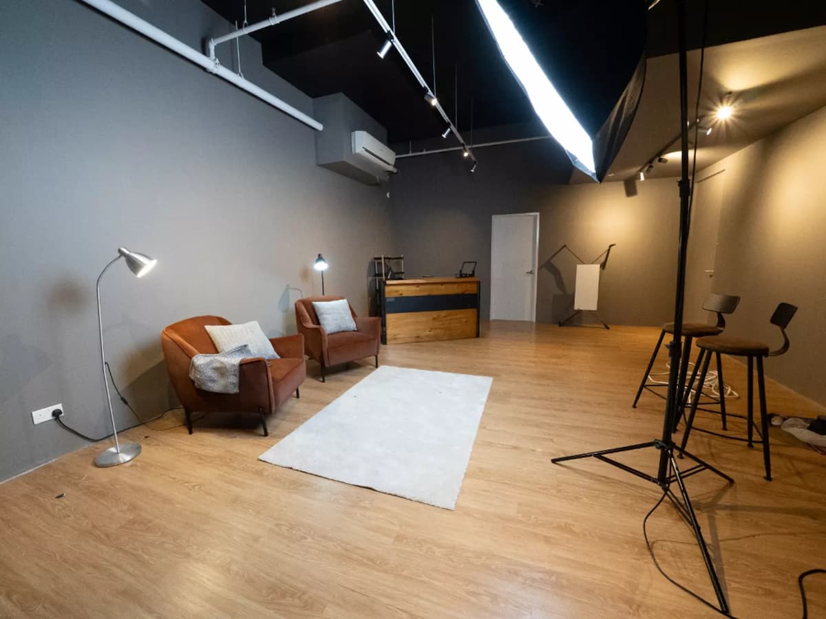 Studio space with armchairs, floor lamps, softbox lighting, and a bar counter against a gray wall.