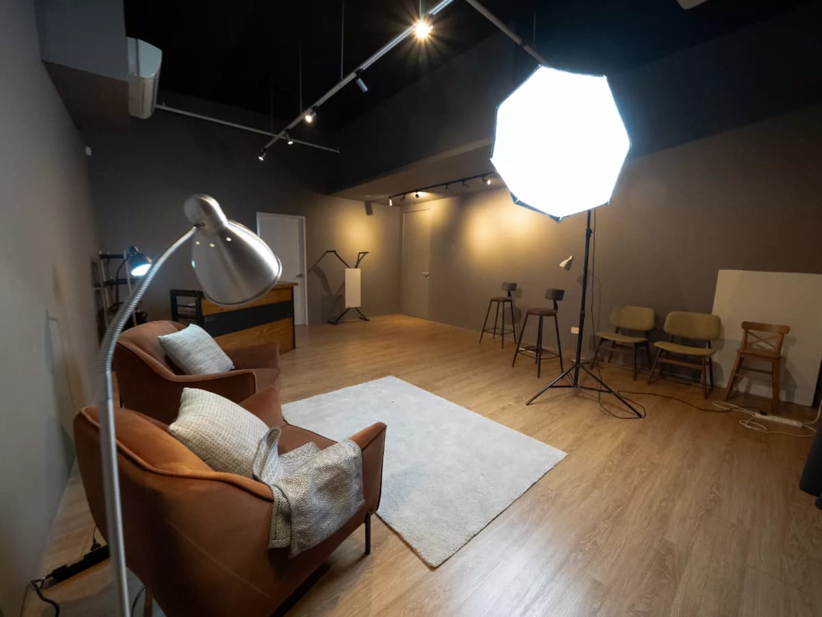 Studio space with armchairs, softbox lighting, stools, and a bar counter on a wood floor.