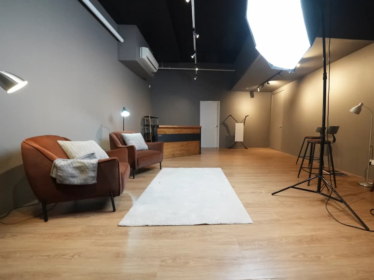 Minimal studio set with armchairs, bar counter, softbox lighting, and a white rug on wood flooring.