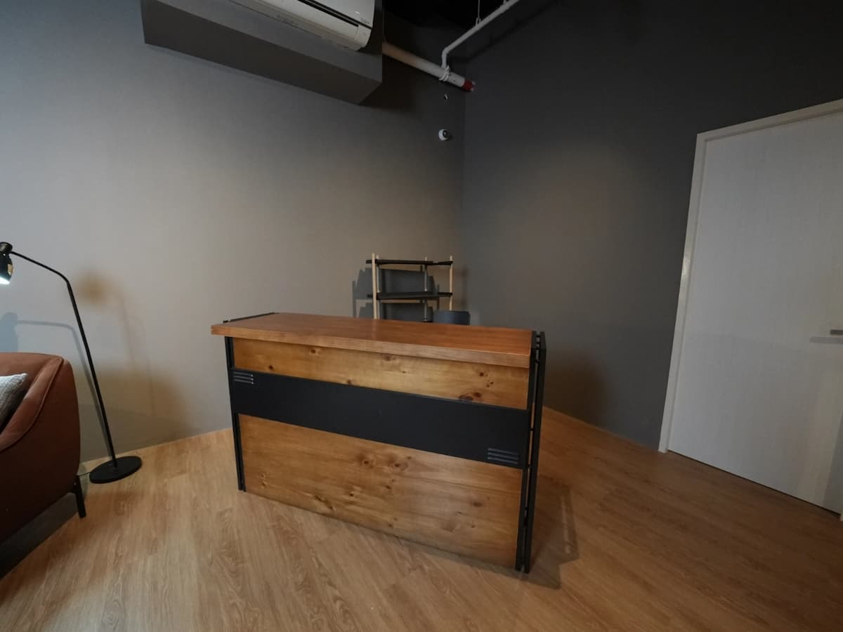 Wooden bar counter against a gray wall with a door and shelving unit in a studio space.