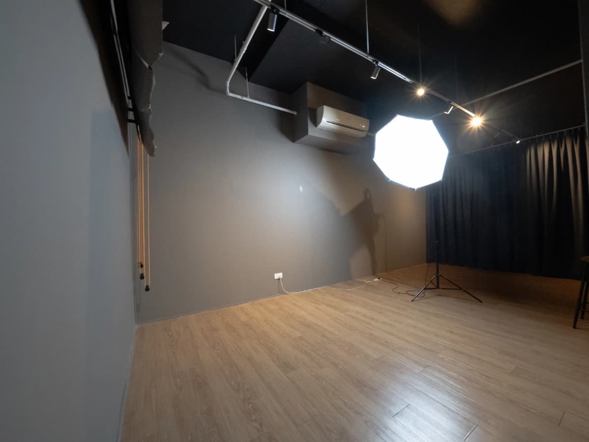 Empty studio corner with gray walls, wood flooring, and a large softbox light set up.
