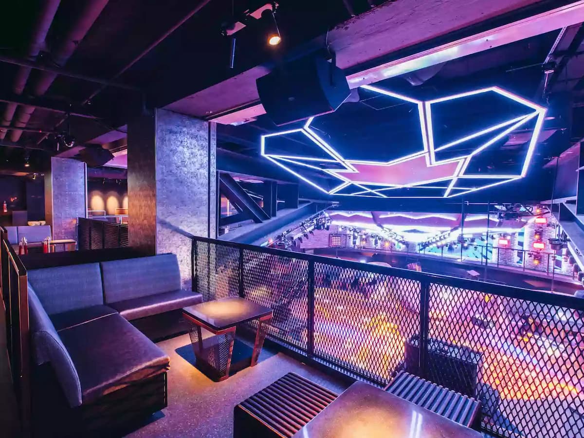 balcony seating overlooking a vibrant nightclub dance floor with geometric LED ceiling lights.