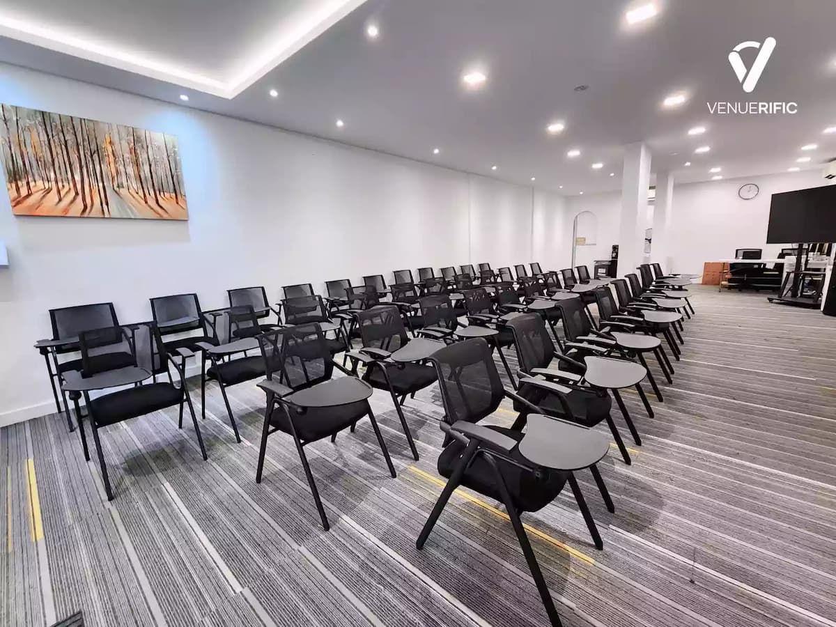 minimalist seminar room with rows of black mesh chairs and a landscape painting on the wall.