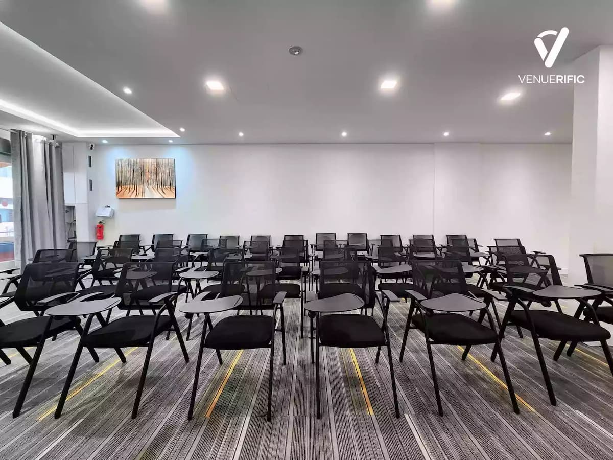 Modern training room with rows of black mesh chairs, tablet-arm desks, grey striped carpeting, and a forest painting on the wall.