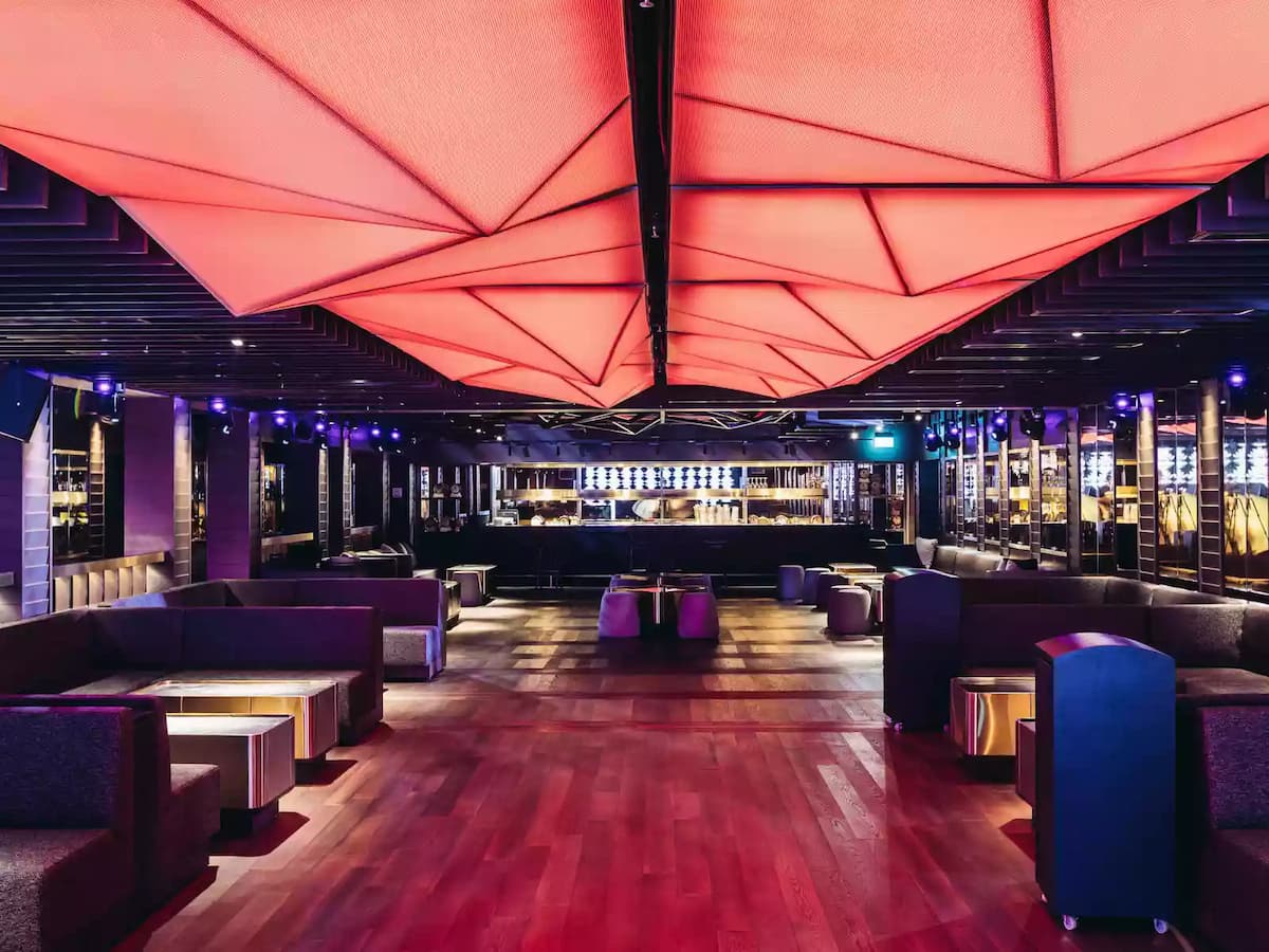 Upscale lounge with red geometric ceiling, plush seating, and ambient bar lighting.