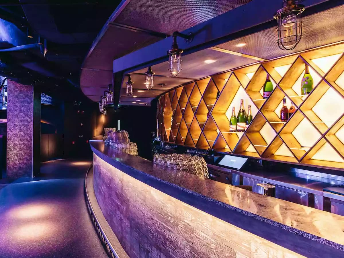 Stylish curved bar with illuminated bottle display, warm accent lighting, and an upscale nightlife ambiance.