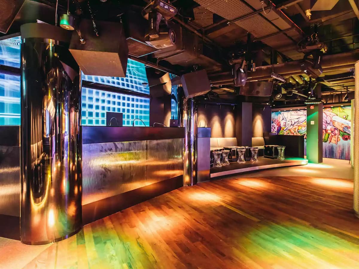 Modern nightclub interior with DJ booth, dance floor, and colorful lighting.