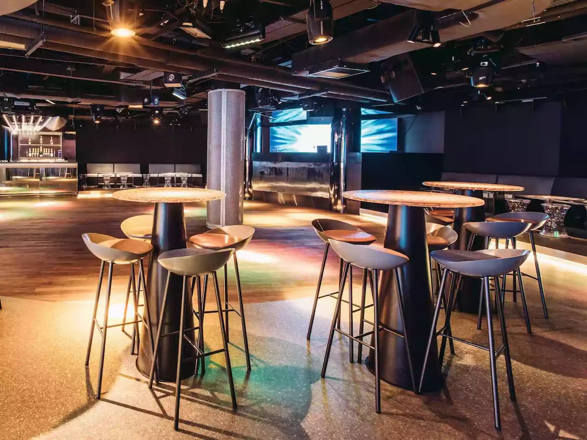 Contemporary event space with high tables, bar seating, and stage lighting.