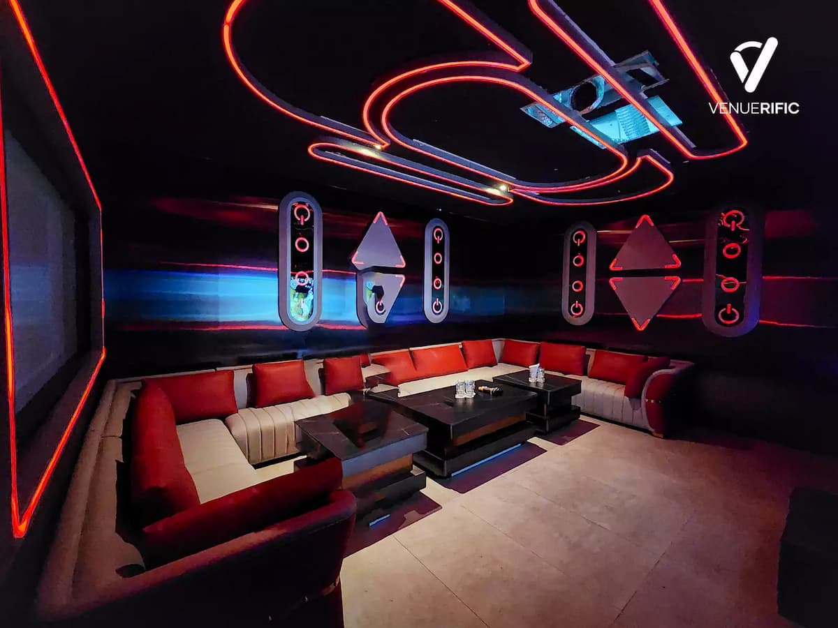 Wide shot of a red-lit private lounge with white sofas and futuristic wall decor.