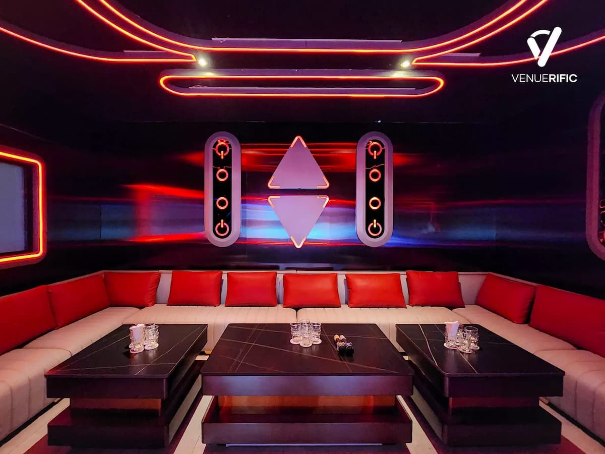 Large screen framed in red neon above white sofas with red pillows.