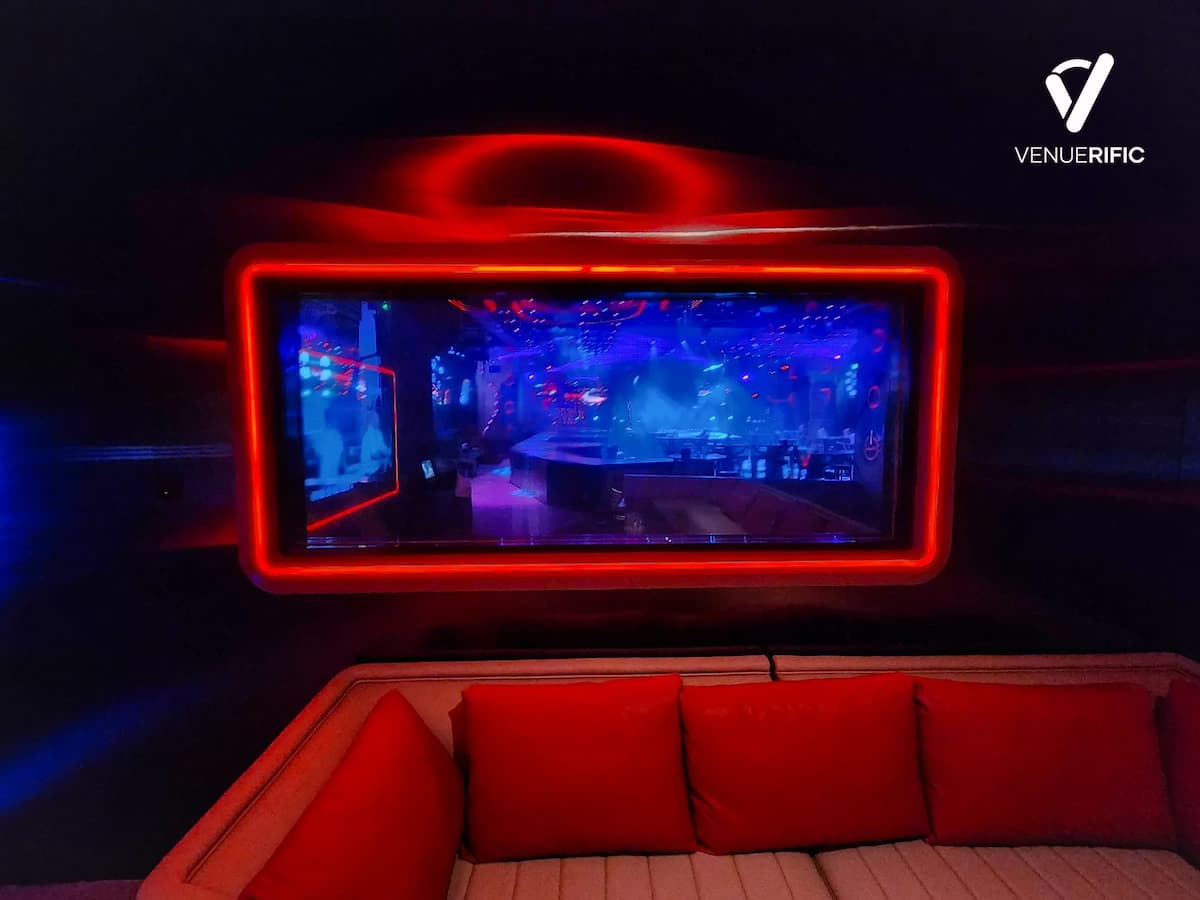 Large screen framed in red neon above white sofas with red pillows.