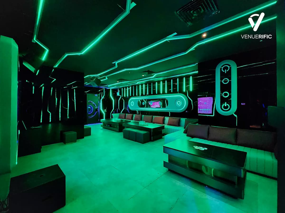 Green-lit futuristic lounge with long sofas and geometric neon wall patterns.
