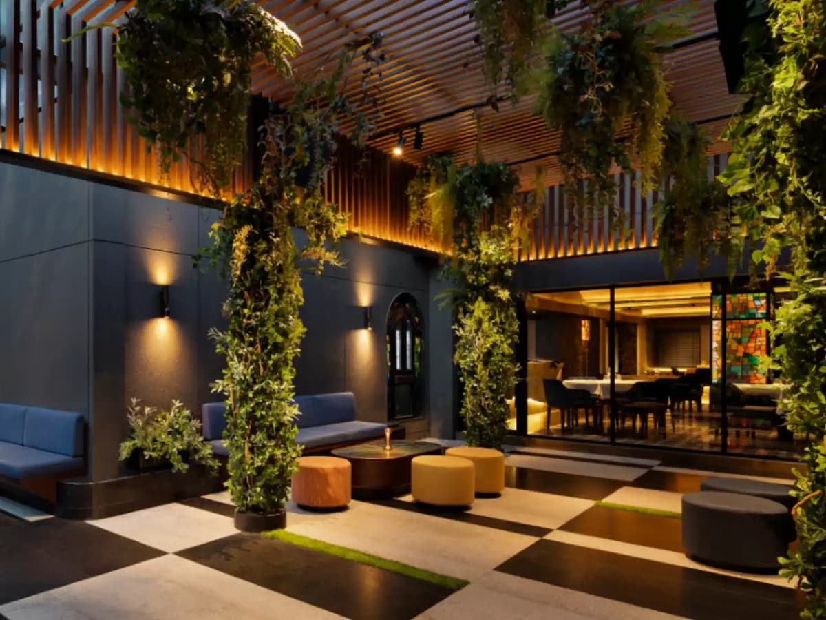 Elegant courtyard-style lounge with hanging greenery, modern seating, and glass doors leading to a private dining room.