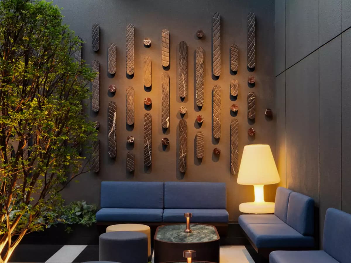 Cozy lounge corner with blue seating, decorative wall art, indoor greenery, and warm floor lamp lighting.