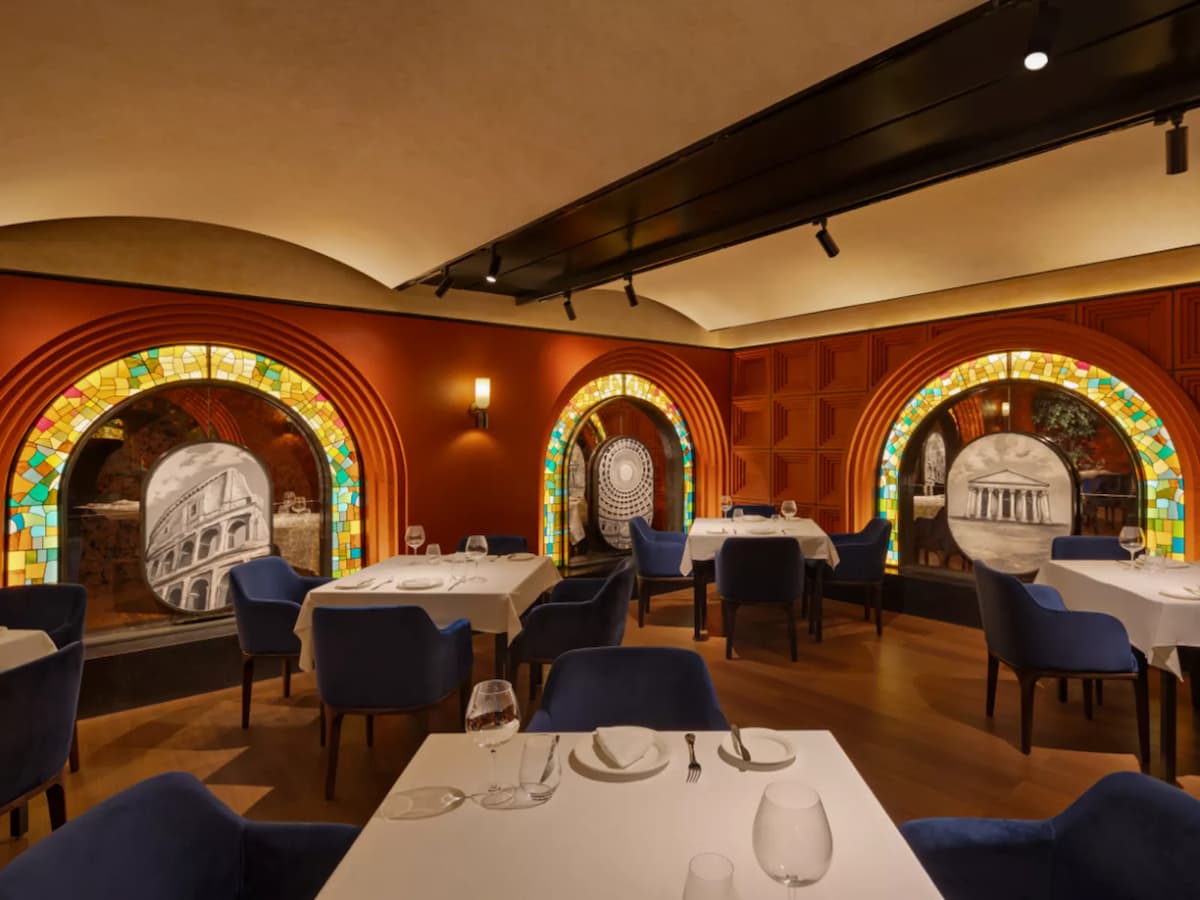 Upscale dining room with white tablecloth settings, blue chairs, and stained glass arched wall features.