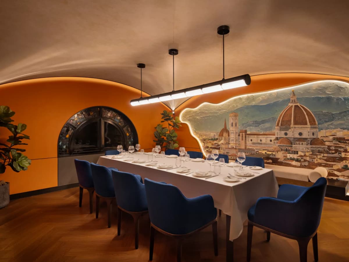Elegant private dining room with long set table, blue chairs, and mural backdrop of a historic city skyline.